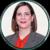 Professional headshot of a woman with shoulder-length brown hair, red lips, wearing a gray blazer over a red blouse with pearl earrings