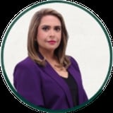 Professional headshot of a woman with shoulder-length brown hair wearing a purple blazer over a black top, on a white background in a circular frame